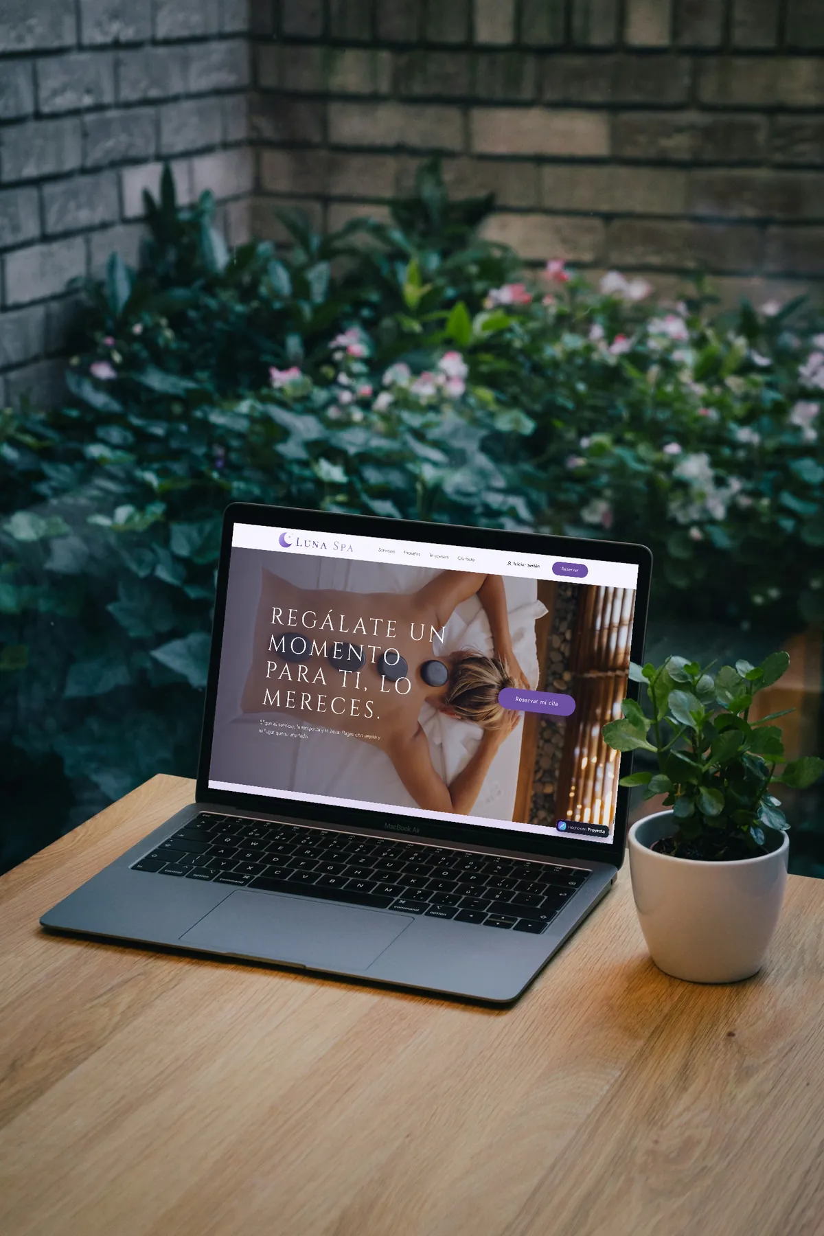 La página de Luna Spa en una laptop sobre una mesa de madera, junto a una planta: «Regálate un momento para ti, lo mereces.» y el botón «Reservar mi cita»